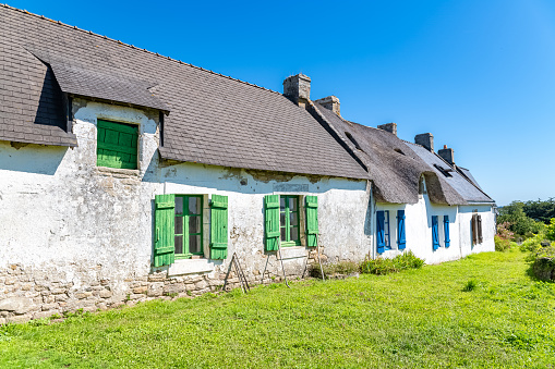 A neat whitewashed thatched roof Irish cottage on the island of Inishee  with wagon wheels and farm cart in front