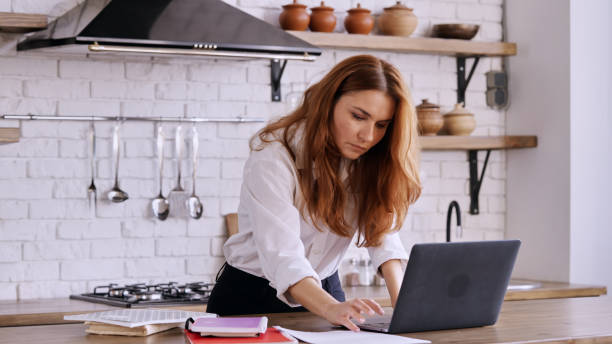 istock Caucasian female working on her laptop in a kitchen 1454964454