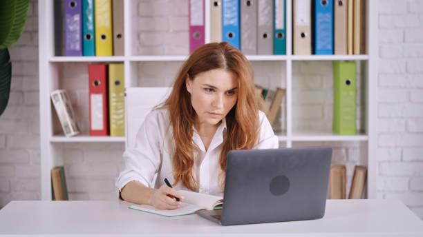 istock Caucasian female working on her laptop and taking notes in a kitchen 1454964475
