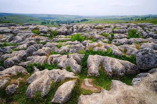 View of Malham Cove limestone formation in background of greenery fields in Yorkshire Dales