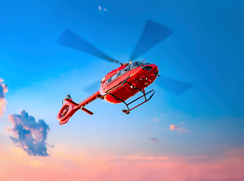 A red medical service helicopter in the air with sunset in the background