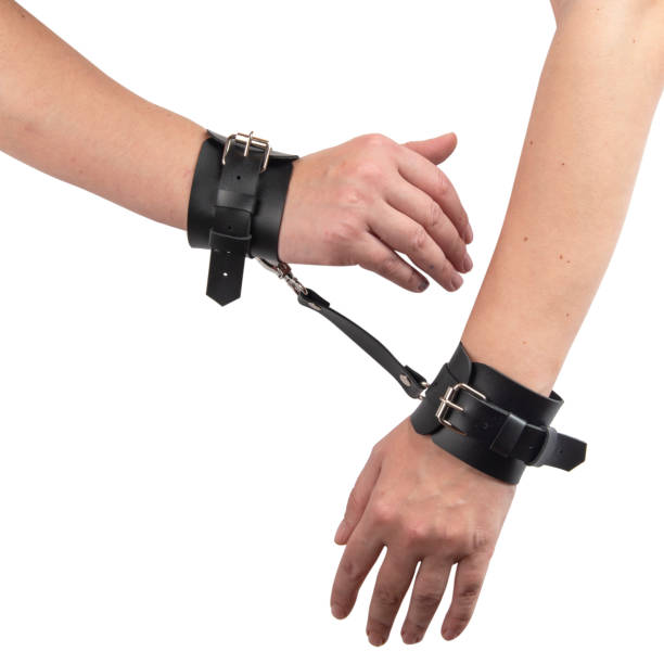 istock Toy black leather handcuffs on hand isolated on the white background 1454976703