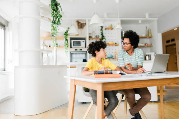 istock Boy writing on a book while his mother working on laptop. Kid studying with mother working from home. 1454977768