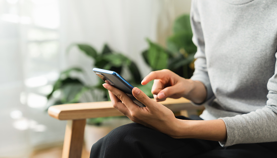 Hand holding smartphone with using social media on internet on sofa in living room.