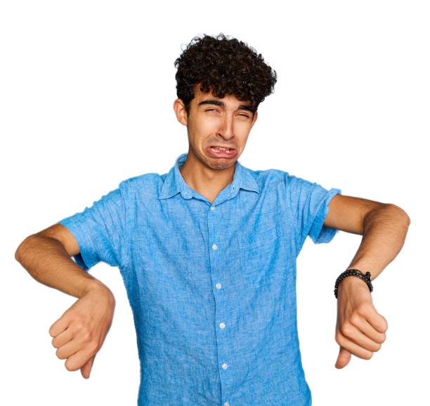 Upset teenage boy with casual clothes and wavy black hair frowning sulking sad, disappointed, show thumbs-down grimacing, give negative opinion, judging bad uninteresting movie, stand white background adolescente molesto con ropa casual y cabello negro ondulado frunciendo el ceño enfurruñado triste, decepcionado, mostrar muecas con el pulgar hacia abajo, dar una opinión negativa, juzgar una mala película poco interesante, pararse fondo blanco