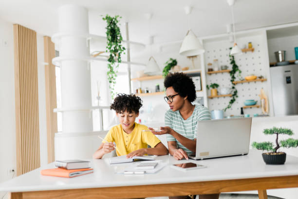 istock Boy writing on a book while his mother working on laptop. Kid studying with mother working from home. 1454980450
