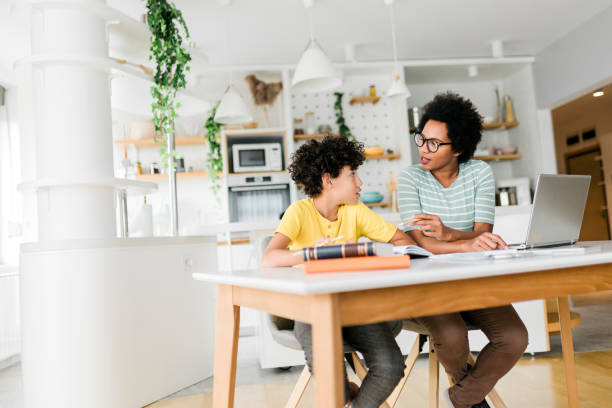 istock Boy writing on a book while his mother working on laptop. Kid studying with mother working from home. 1454980465