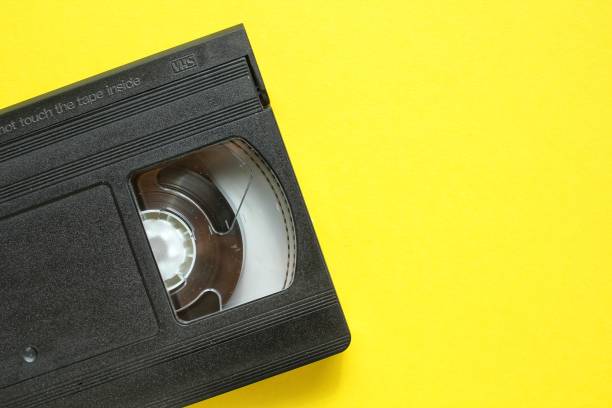 istock Black VHS videotape recorder cassette on yellow background. Old obsolete technology for tape recording and watching media movies 1454981779