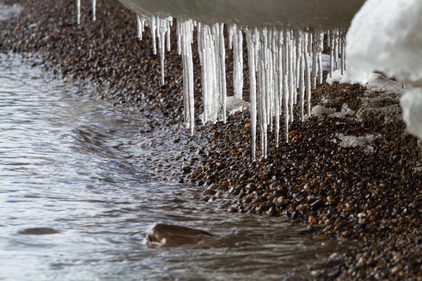 icicles hang from a coastal ice floe over a pebble beach - floe lake imagens e fotografias de stock