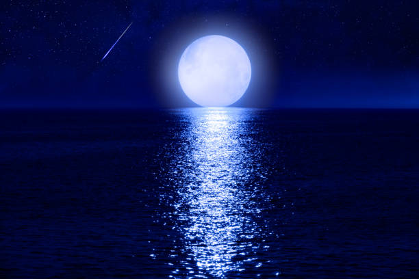 istock Full Moon with starry skies rising above ocean horizon. 1454983152
