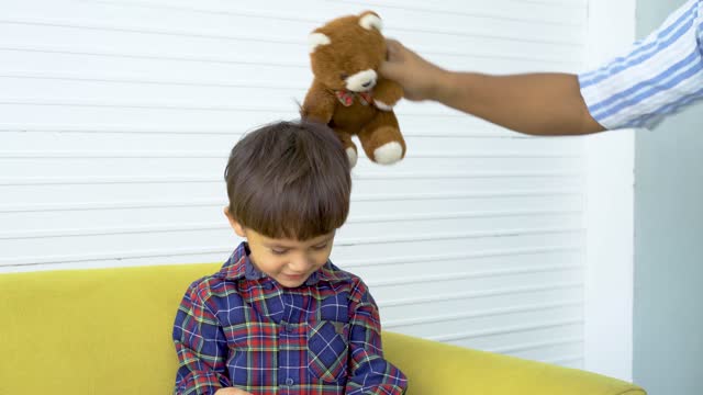 Caring father giving teddy bear and play with his son by bringing the bear to touch the face in order to pay attention to the gift his father gave