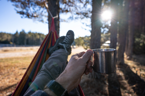 Tourist lying in hammock with cup of coffee in hand on a sunny day in nature.