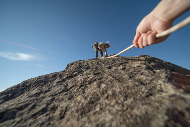 Mountain climber with climbing equipment (rope, backpack, helmet, hood,...) against the sun and blue sky. Climbing up the mountain.