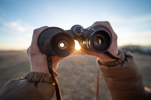 Hands holding binoculars while at high point view towards the sunset.