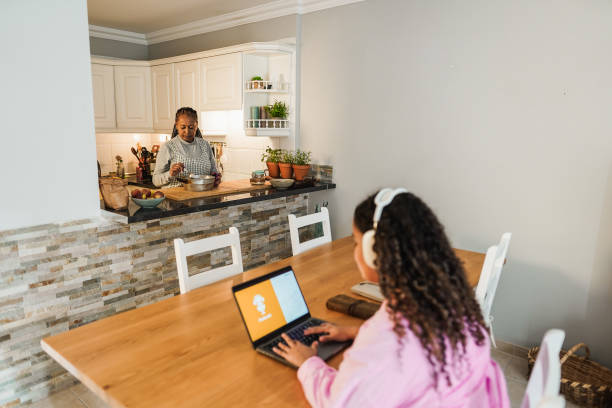 istock African daughter using laptop while mother cooking in kitchen at home - Soft focus on senior woman face 1454991200
