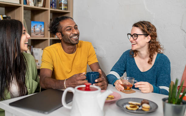 Young friends hangout in coffee shop, multiracial universitary student having fun at breakfast, happy people taking a break in cafeteria to drink coffee and eat cakes before starting all activities stock photo