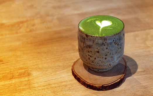 Heart shape matcha green tea in a Japanese style cup on wooden desk warm light tone
