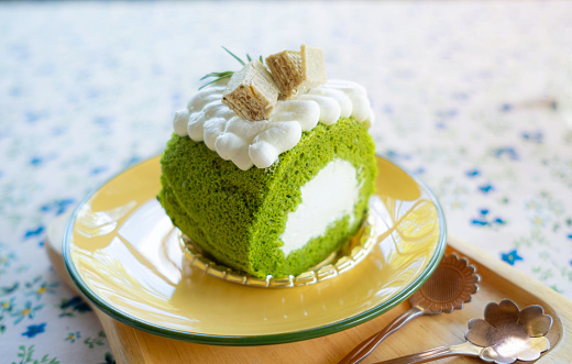 Matcha roll cake decorated with whipped cream on top. Wan in a light brown dish