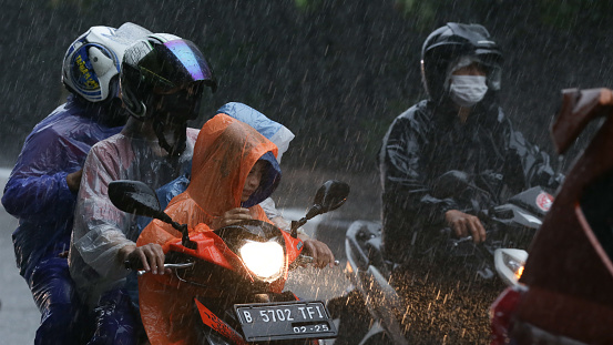 People riding motorbikes in the rain: Jakarta, Indonesia - November 12, 2022: