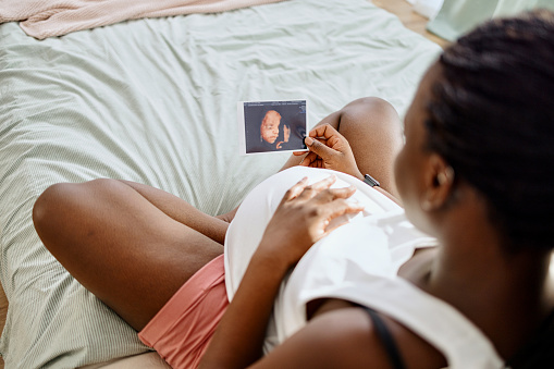 Pregnant woman sitting on the bed in her bedroom watching sonogram