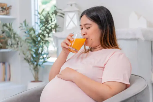 Asian pregnant woman drinking orange juice and stay at home alone. family lifestyle.