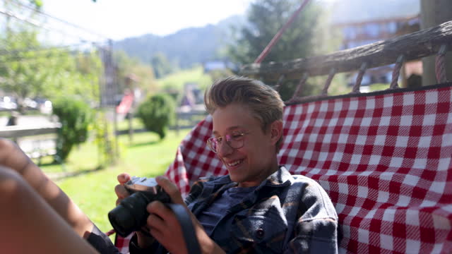 Teenage boy resting on hammock and reviewing photos on a retro mirrorless camera