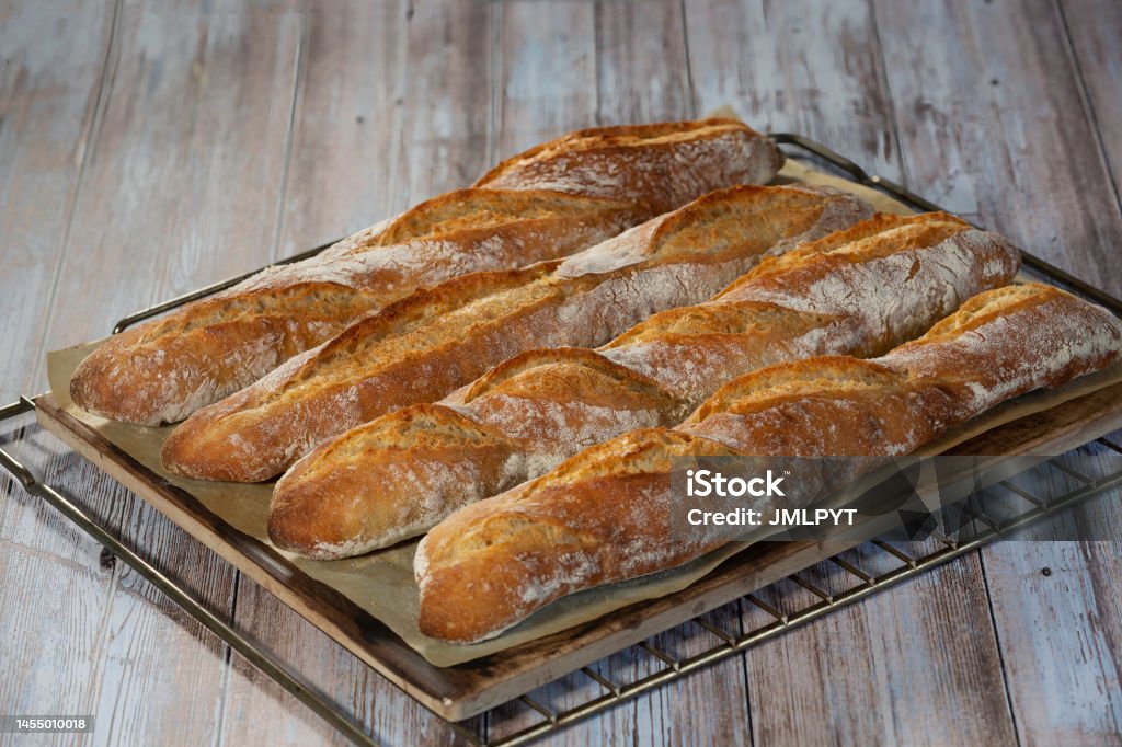 Traditional sourdough bread on a wire rack on a wooden table Four homemade sourdough bread sticks placed on a wire rack. The baguettes are placed on a baking sheet. Cutout objects, place for text. Artisanal Food and Drink Stock Photo