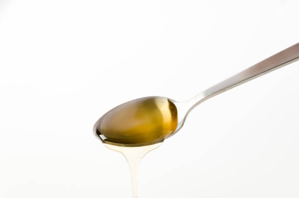 Metal spoon pouring fresh honey on white background
