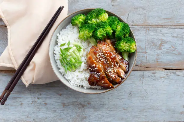Teriyaki chicken has rice and broccoli vegetable in bowl on wood background, top view, healthy food concept.