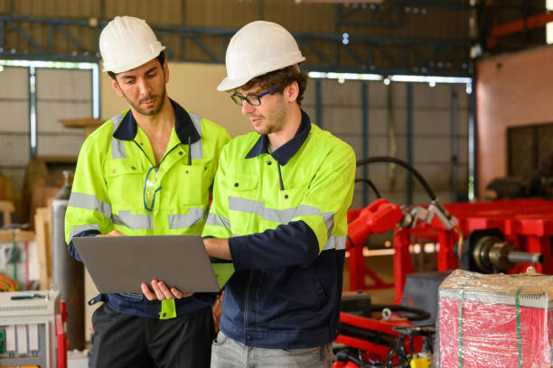 istock Two technicians workers with safety uniform using laptop talking and controlling machinery at manufacturing area of industrial factory 1455012498