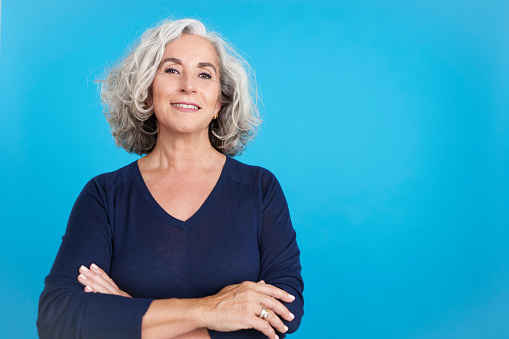 Studio portrait with blue background of a proud mature woman looking at camera with arms crossed