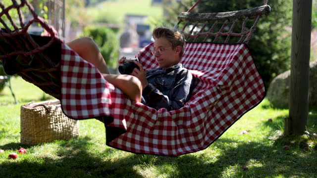 Teenage boy resting on hammock and reviewing photos on a retro mirrorless camera