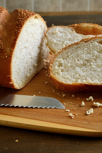 closeup sesame seed loaf of bread on cutting board with serrated knife
