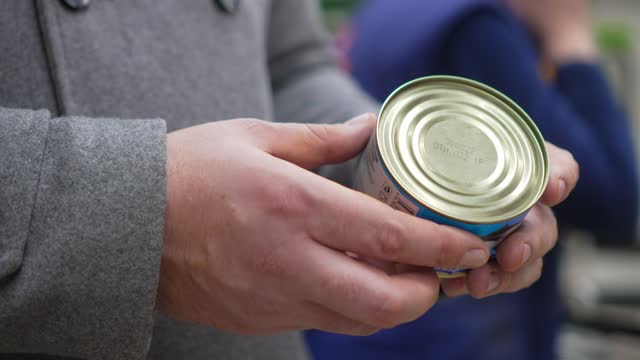 Hands in hand holding canned food read expiration date of composition.