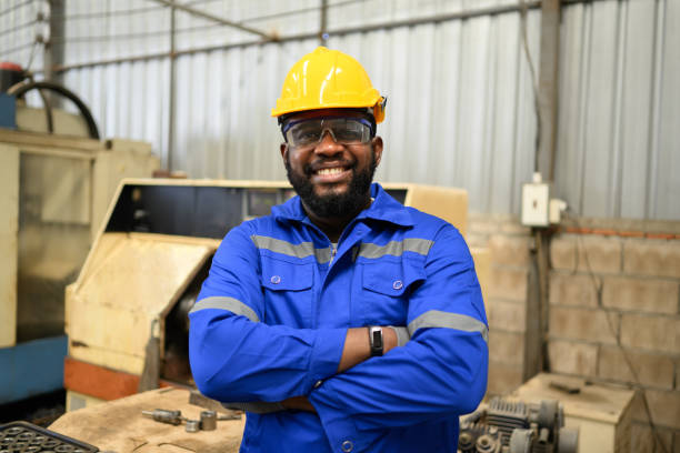 retrato de un ingeniero trabajador seguro de sí mismo sonriendo y trabajando en la fábrica - african descent factory accuracy analyzing fotografías e imágenes de stock