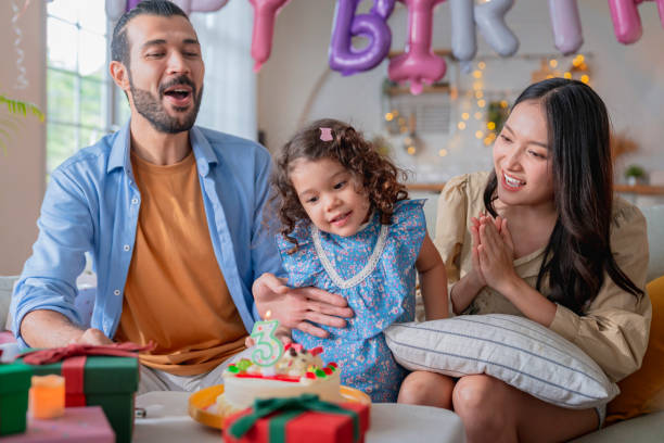 festa de aniversário da filha de 3 anos celebra em casa, toda a família ajudando-a a soprar as velas em balões da sala de estar e cores itens decorativos está por toda parte, menina é grande risada sorrindo alegria - 2 3 years children only group of people enjoyment - fotografias e filmes do acervo