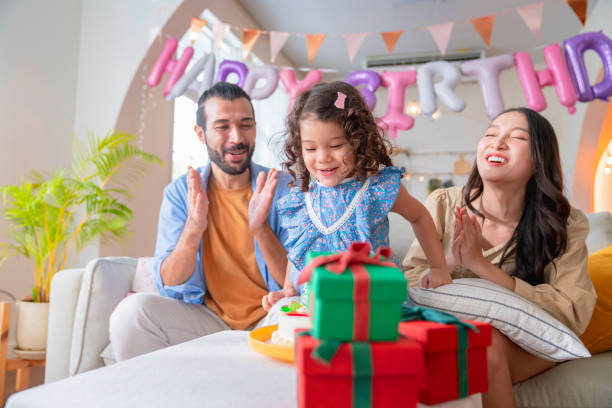 hija cumpleaños 3 años fiesta celebrar en casa, toda la familia ayudándola a soplar las velas en globos de la sala de estar y colores artículos decorativos está por todas partes, la niña es una gran risa sonriendo alegría - 2 3 years children only group of people enjoyment fotografías e imágenes de stock