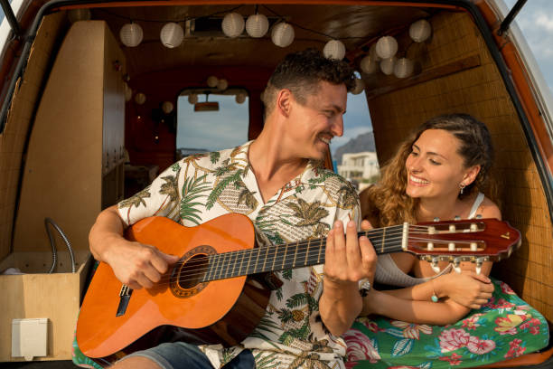 istock Man playing the guitar next to a woman inside a camper van 1455018544