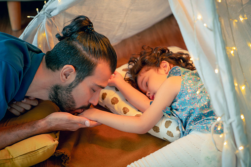 Lovely concept,Multiracial Parents kiss their little joyful daugher tender while her girl fall in sleep lying on the floor after playing all day long with care tenderness,family relation love happy