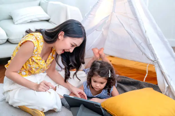 happiness lifestyle at home ,asian female woman nanny aupair takecare teach online study to little child girl with cheerful laugh smiling in living area at home morning weekend peaceful online study