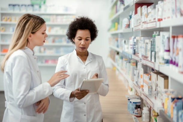 Two Mixed Race Female Pharmacist Talking in Pharmacy Drugstore Pharmacy Drugstore: Two Mixed Race Female Pharmacist Chemist Working in Pharmacy Drugstore healthcare and medicine business hospital variation stock pictures, royalty-free photos & images