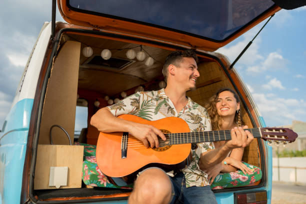 istock Couple enjoying while playing the guitar in a road trip with a retro van 1455018773