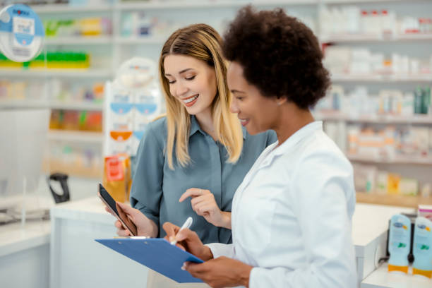 Customer Showing Mobile Phone to African American Female Chemist Pharmacy Drugstore: Young Female Customer Showing Mobile Phone to African American Female Chemist in Pharmacy healthcare and medicine business hospital variation stock pictures, royalty-free photos & images