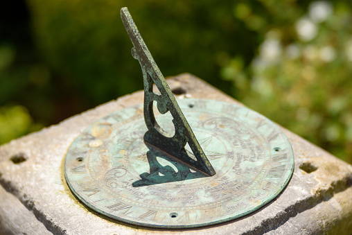 A close-up of an old metal sundial featuring Roman numerals with verdigris casting a shadow  in the afternoon sun