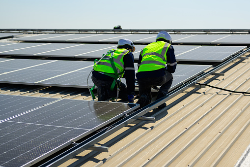 Engineer and technician using laptop checking and operating solar panels system on rooftop of solar cell farm power plant, Renewable energy source for electricity and power, Solar cell maintenance concept