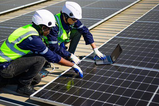 Engineer and technician using laptop checking and operating solar panels system on rooftop of solar cell farm power plant, Renewable energy source for electricity and power, Solar cell maintenance concept