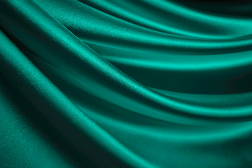 Blue green silk satin. Emerald curtain. Drapery. Shiny fabric. Elegant background for design. Liquid, wave, ripple effect. Beautiful soft folds.