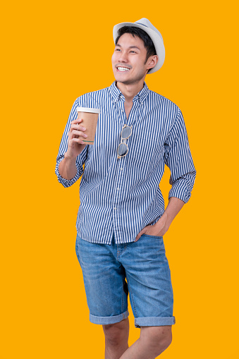 casual traveller male adult wear hat  relax leisure hand hold coffee cup standing with cheerful facial expression studio shot on yellow colour background