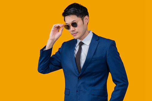 Confident stylish attractive young asian businessman wearing formal blue colour suit and sunglasses,handsome attractive asia male business guy take off sun glasses studio shot