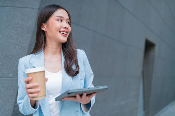 istock smart casual business female woman formal cloth hand hold coffee cup while checking work project schedule on tablet while walking in office building corridor,smile cheerful asian woman walking outdoor 1455022371